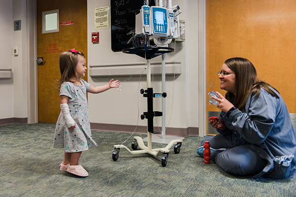 Child life specialist at Marshfield Children's Hospital blows bubbles with anesthesia mask to help 22-month-old master surgery