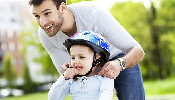 dad helps his child put on bike helmet properly