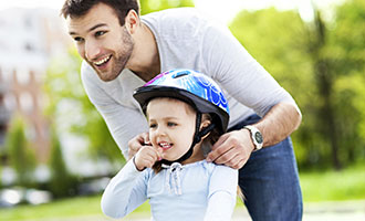 dad helps girl put on bike helmet